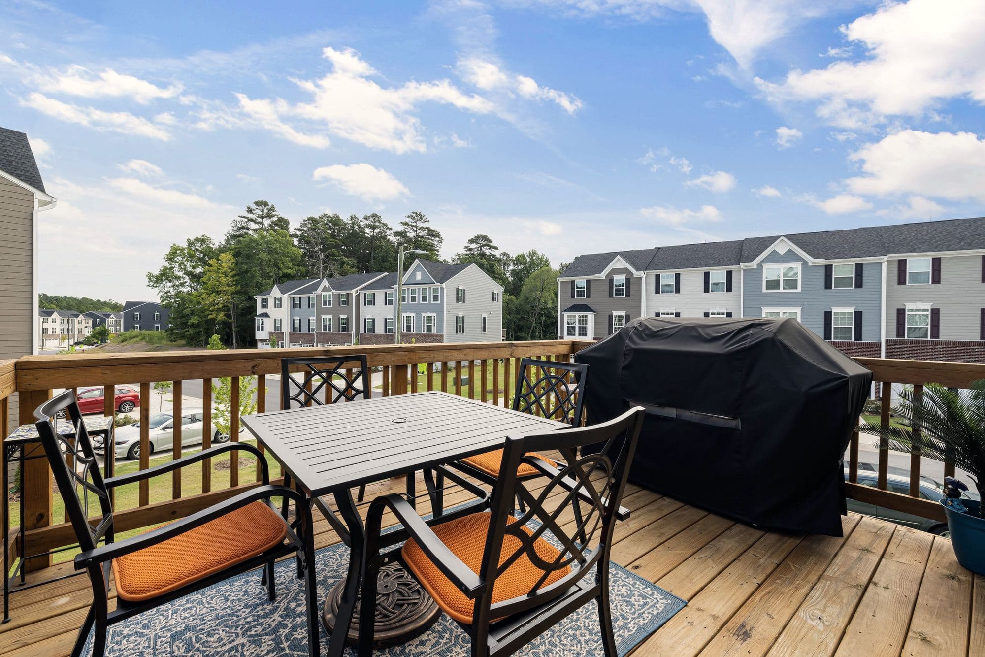 Wood deck with railings, a patio table and a covered grill behind a home