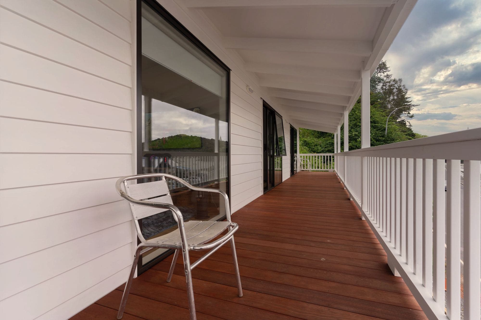 Stained wood deck boards running along a covered porch with a white railing