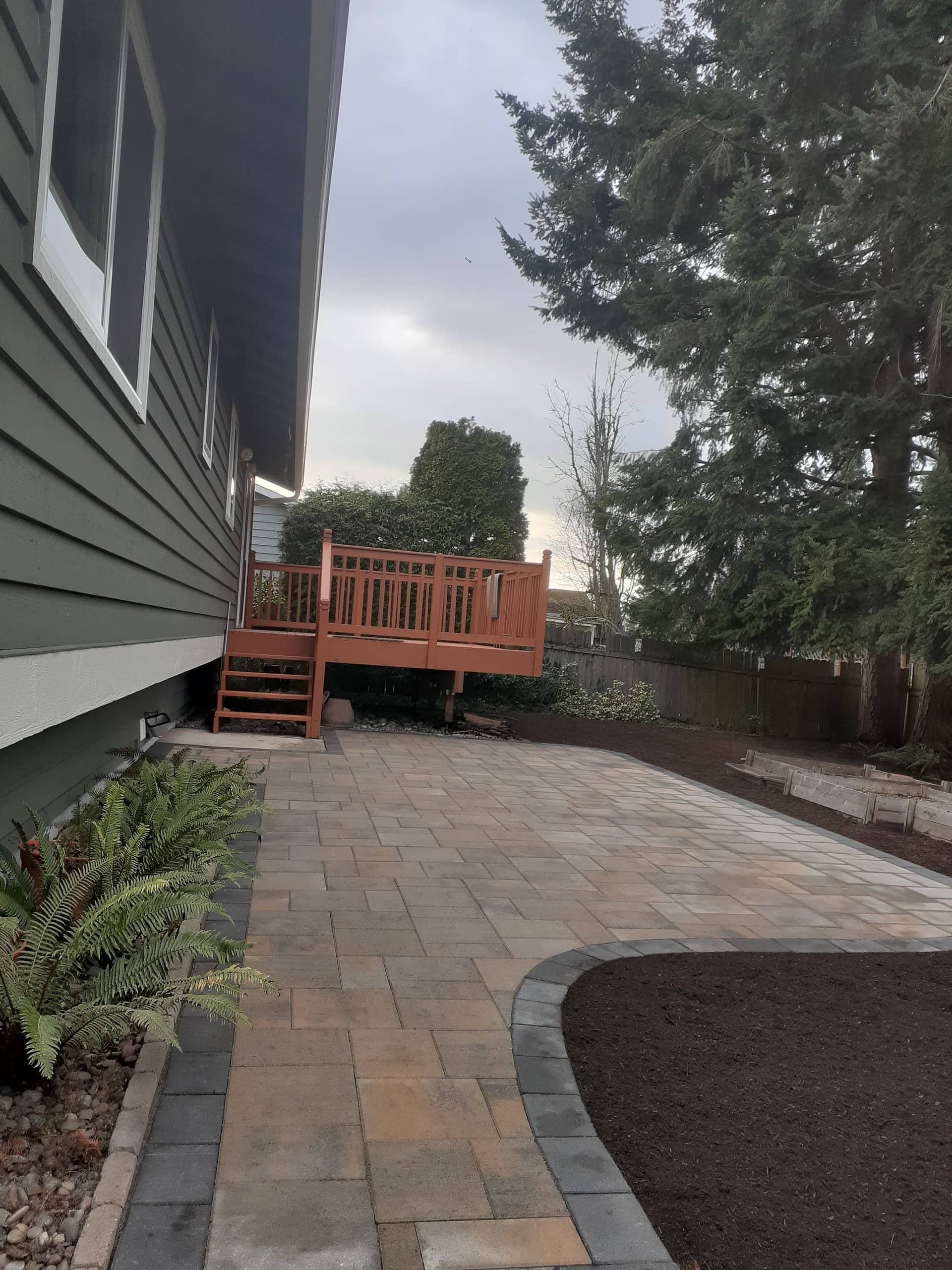 Multi-tone paver patio with curved border, deck in background