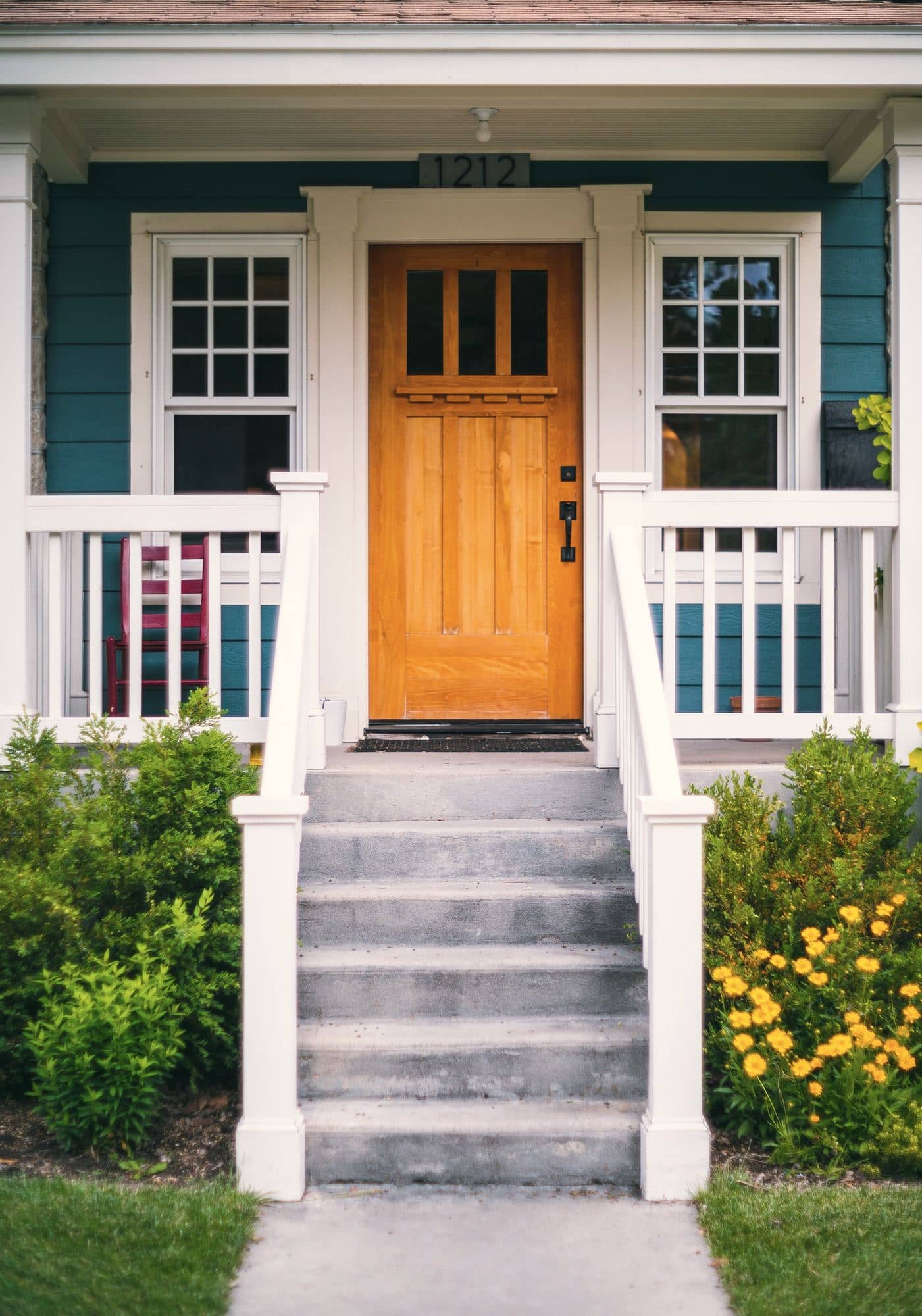 Wood entry door on a teal lap-sided house, reached by concrete steps between white porch railings