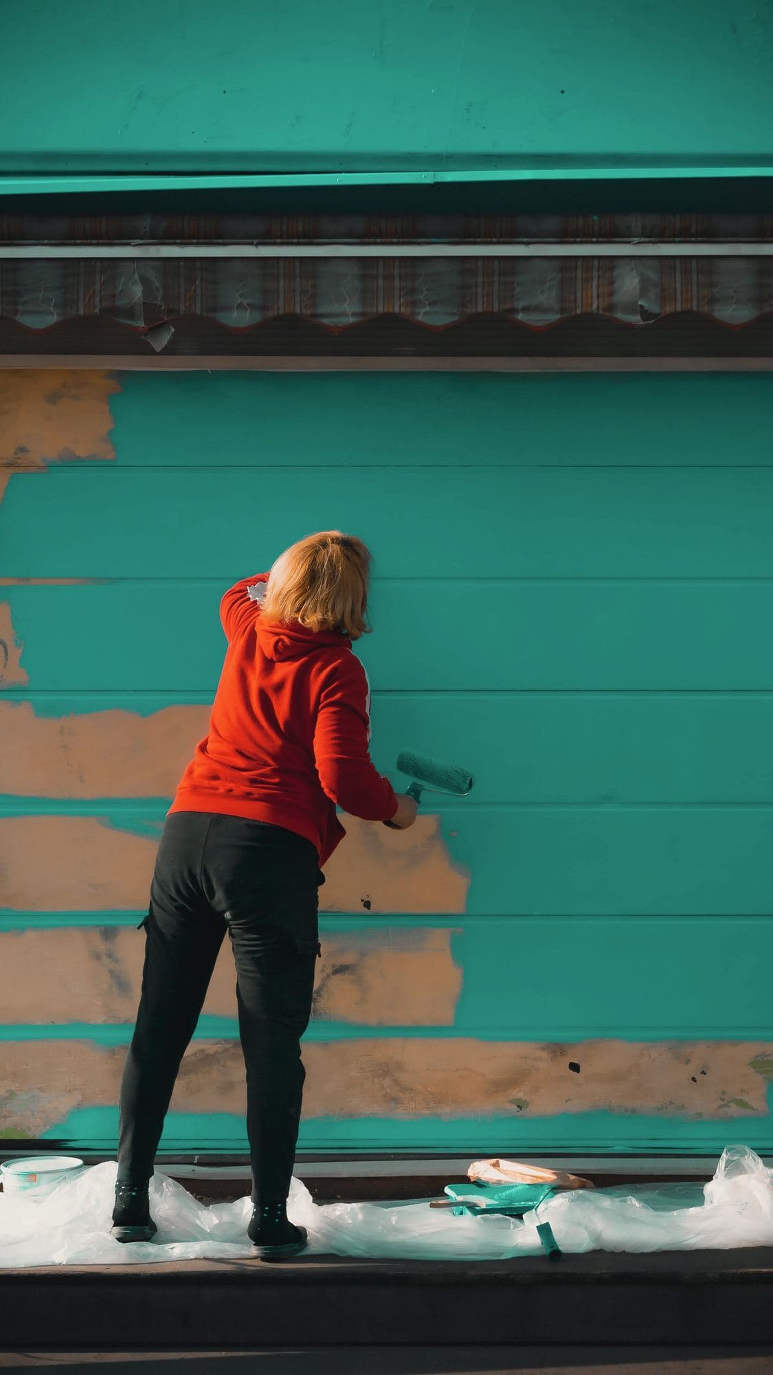 Painter rolling fresh color onto the lap siding of a house, bare wood still showing below
