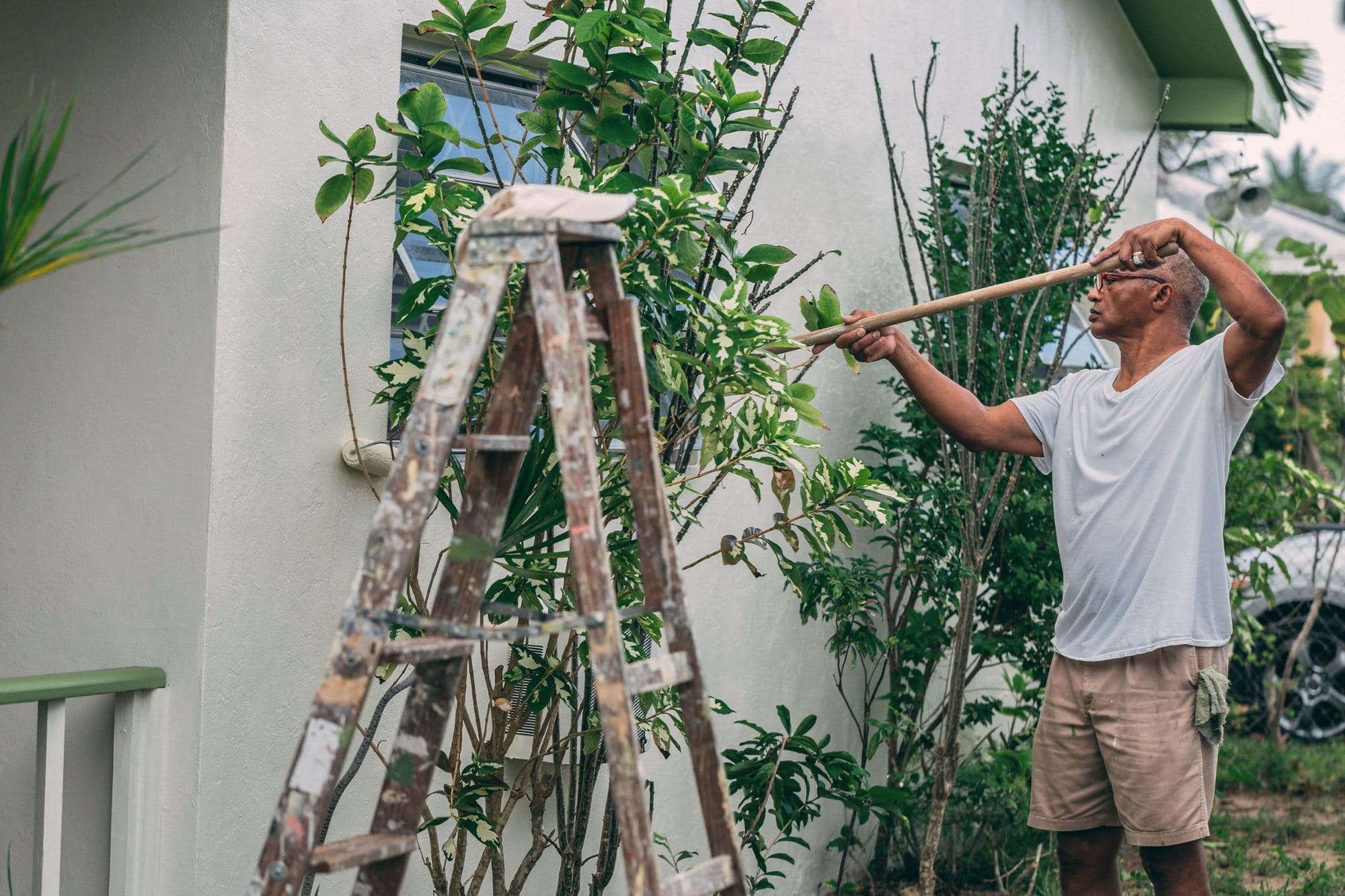 Painter using an extension roller on an exterior house wall beside a stepladder
